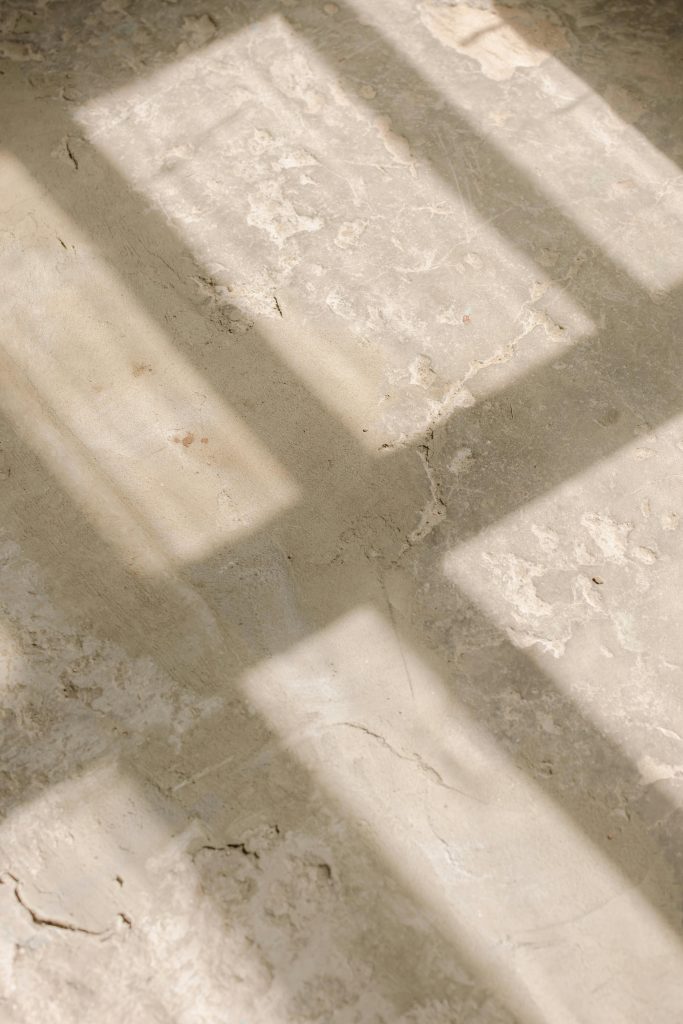 Abstract view of sunlight casting window shadows on a textured concrete surface, creating a grunge aesthetic.