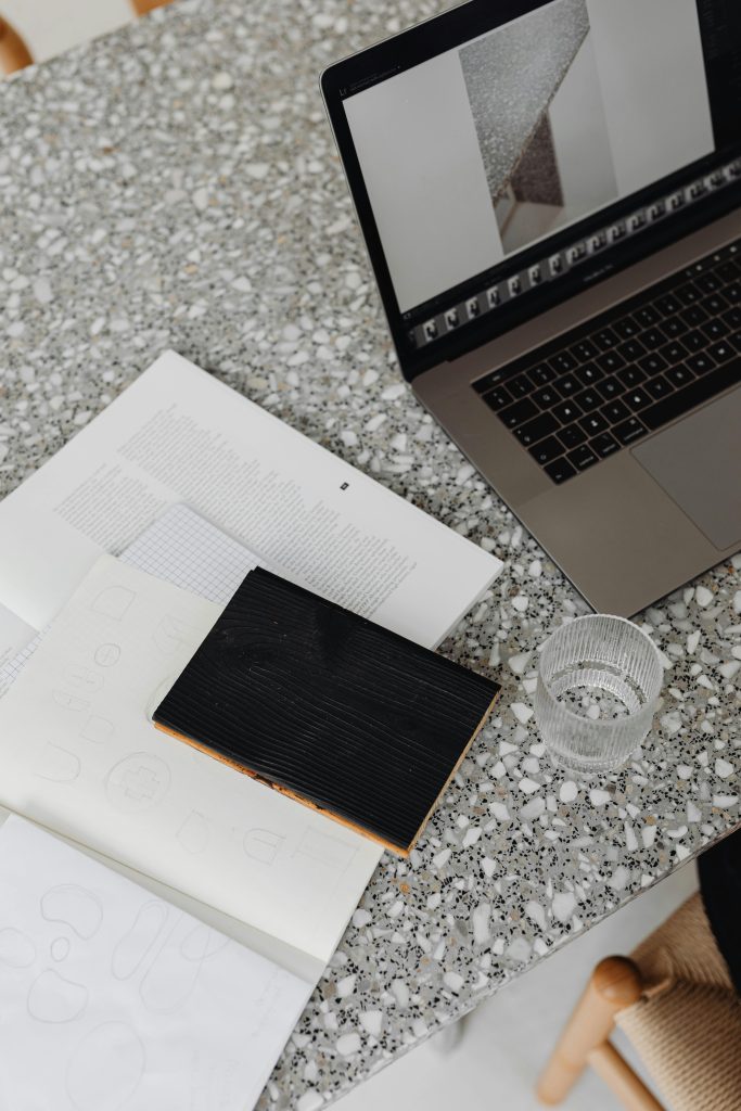 Stylish desk setup with laptop, documents, and glass on terrazzo surface. Perfect for work inspiration.