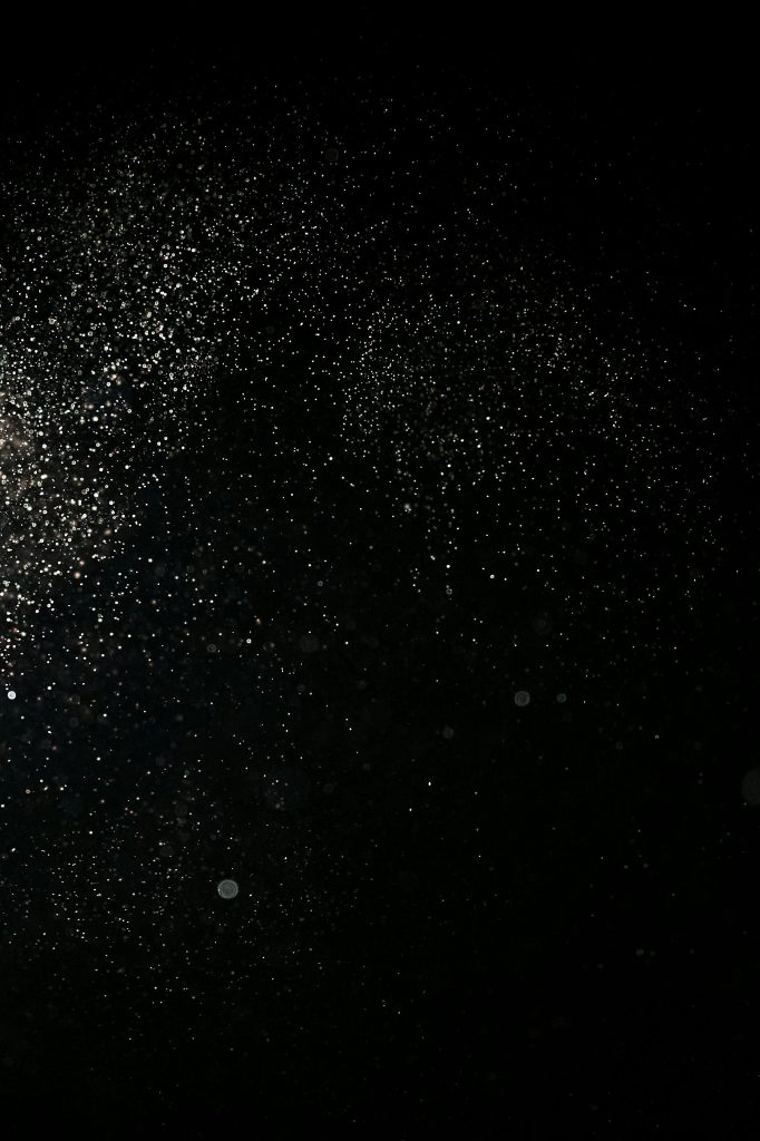 Abstract image of shimmering particles resembling a starry night sky on a black background.